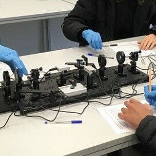 Drei Personen mit blauen Handschuhen bedienen technische Geräte.